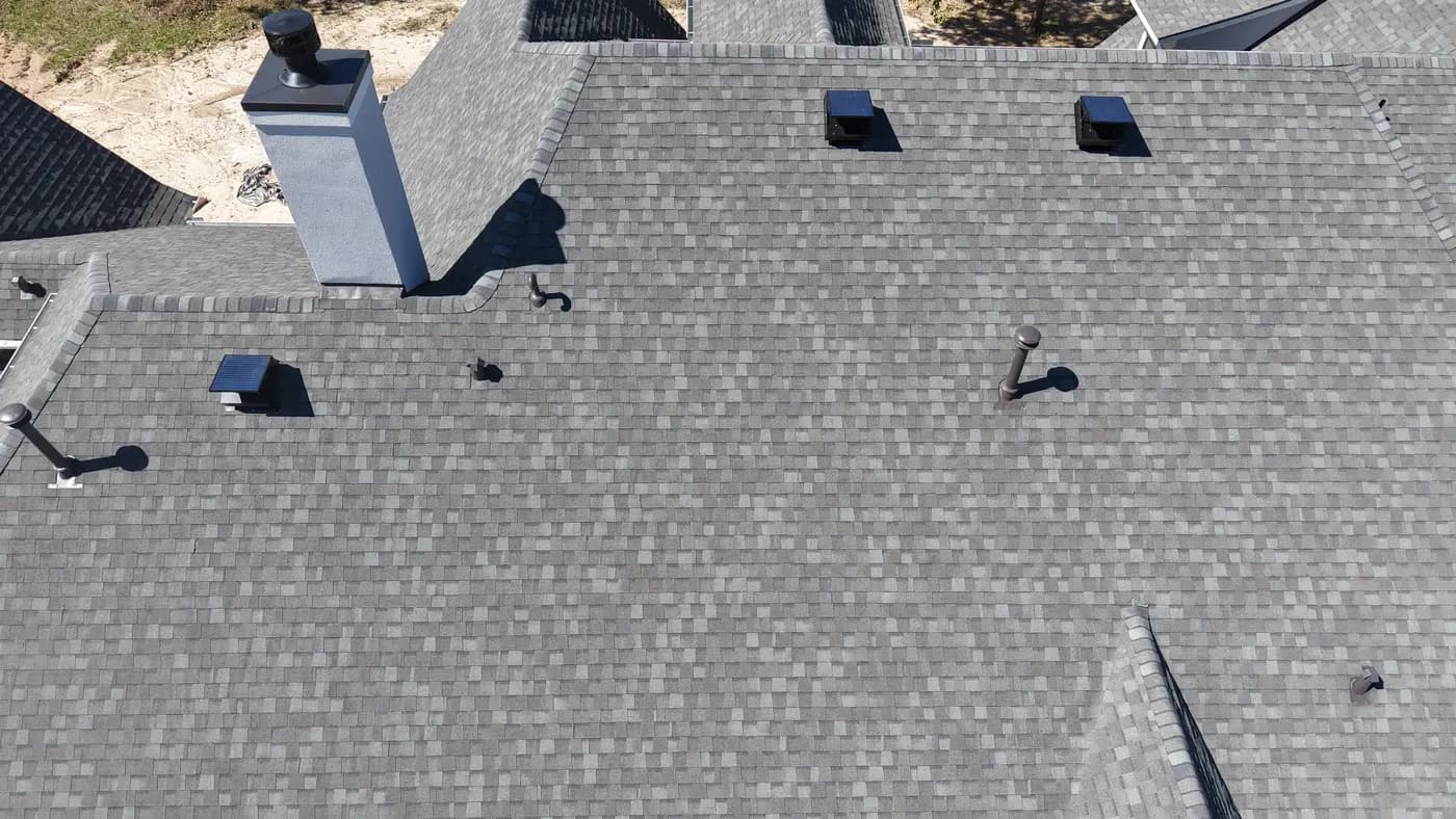 Drone shot of a residential roof with dark asphalt shingles in summer sun